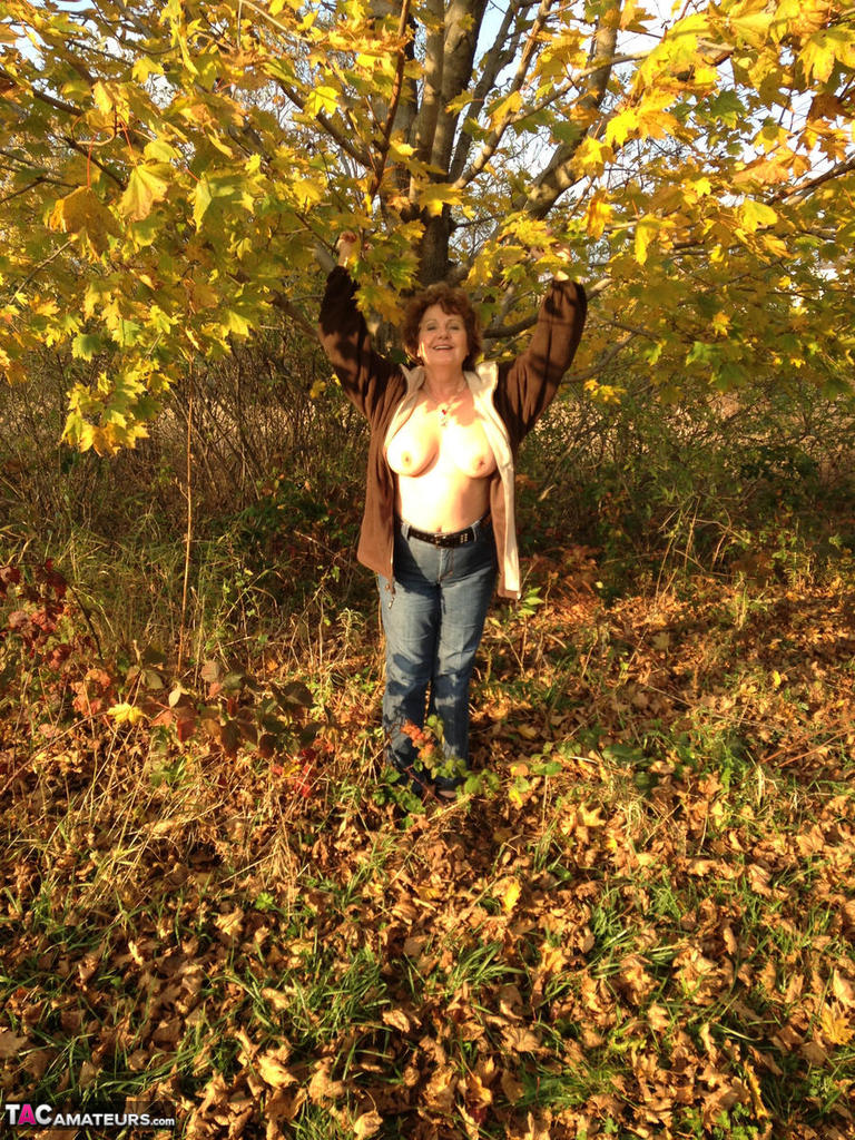 In front of a tree, Busty Bliss, an older woman, displays her large natural breasts.