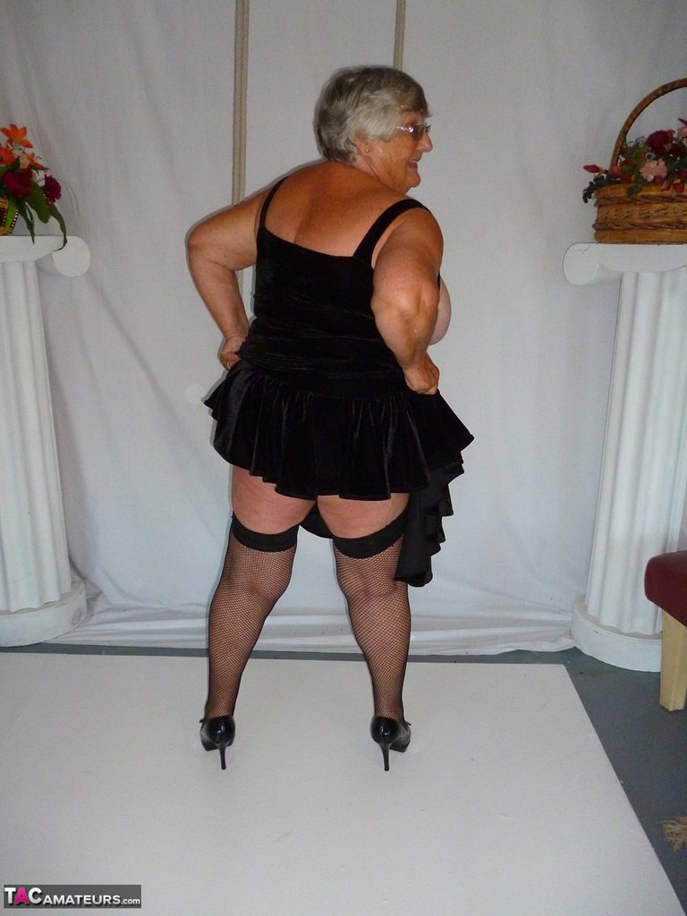 Grandma Libby, who is fat, removes her clothing from a black dress and models herself in stockings.