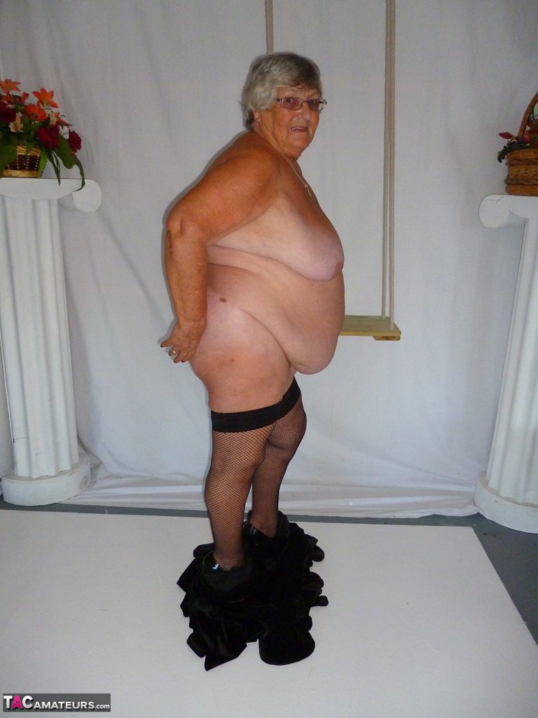 Wearing a black dress and stockings, Grandma Libby poses for the camera in a nude picture.