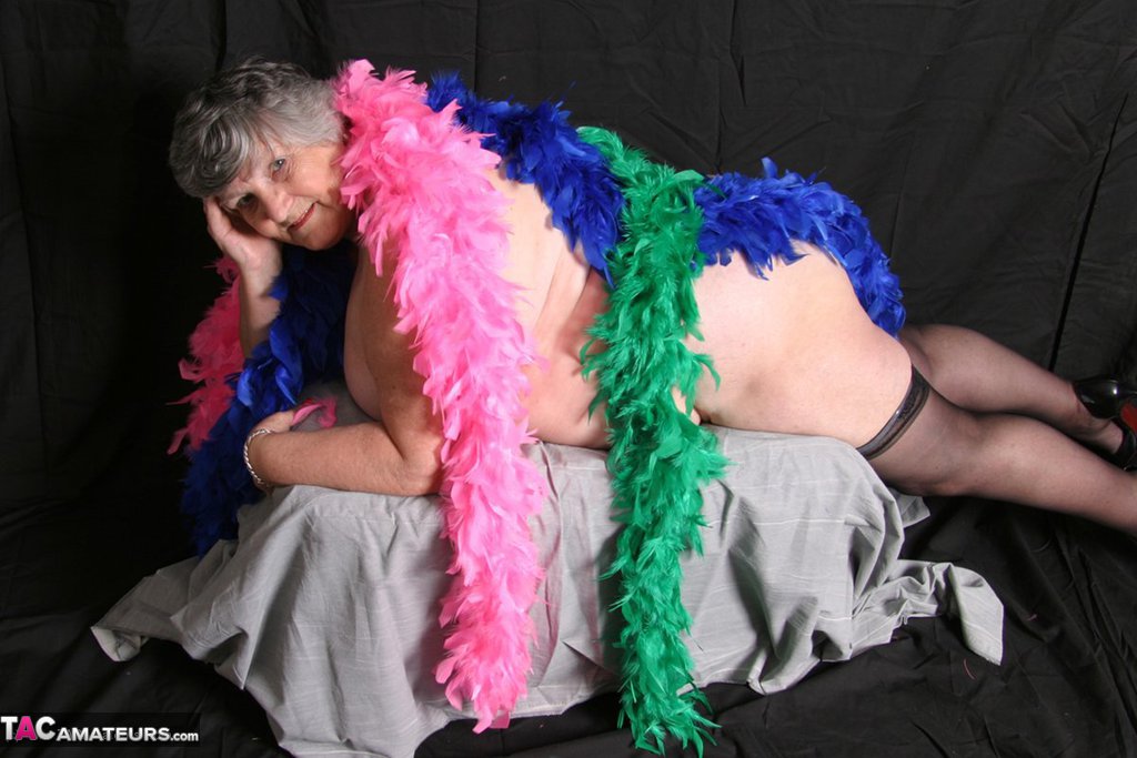 Grandma Libby, who is fat and shows her big tits while wearing feather boas, poses for a photo.