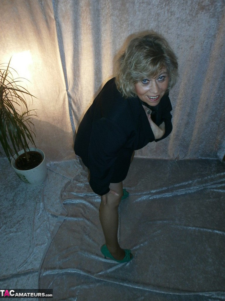 Caro, a self-proclaimed blonde, removes a blazer to expose herself in a bra and pantyhose while naked.