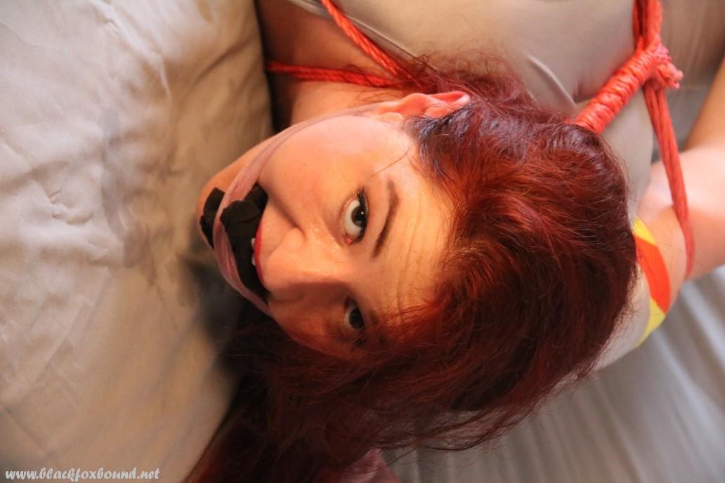 The natural redhead is left on a bed, tied up and gagged.