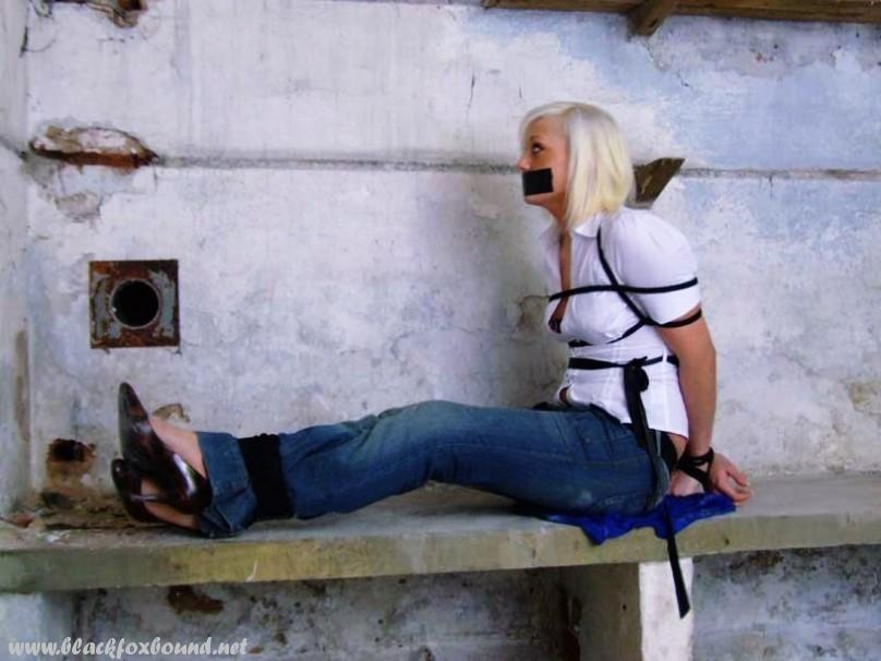 In a pair of blue jeans and white shirt, a British woman is tied up and gagged.