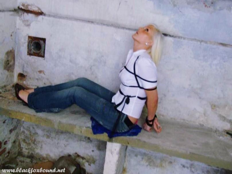 In a pair of blue jeans and white shirt, a British woman is tied up and gagged.