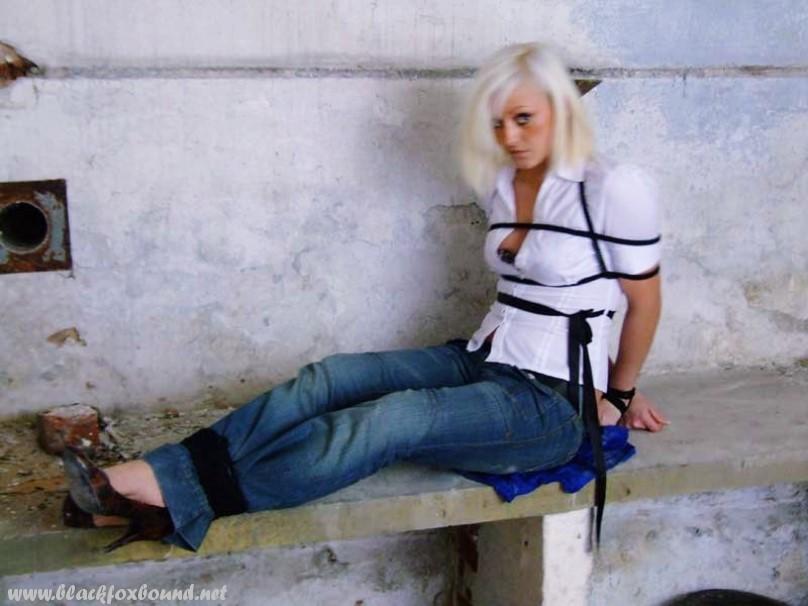 A white shirt and blue jeans are worn by a British woman who is tied up and gagged.