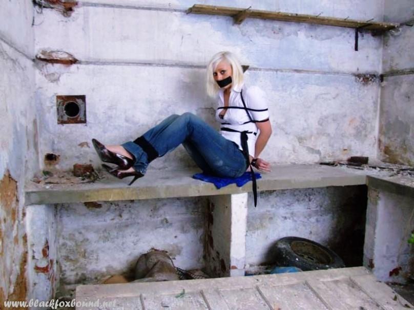 A white shirt and blue jeans are worn by a British woman who is tied up and gagged.