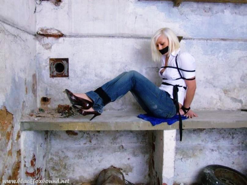 Blue jeans and a white shirt are worn by a British woman who is tied up and gagged.