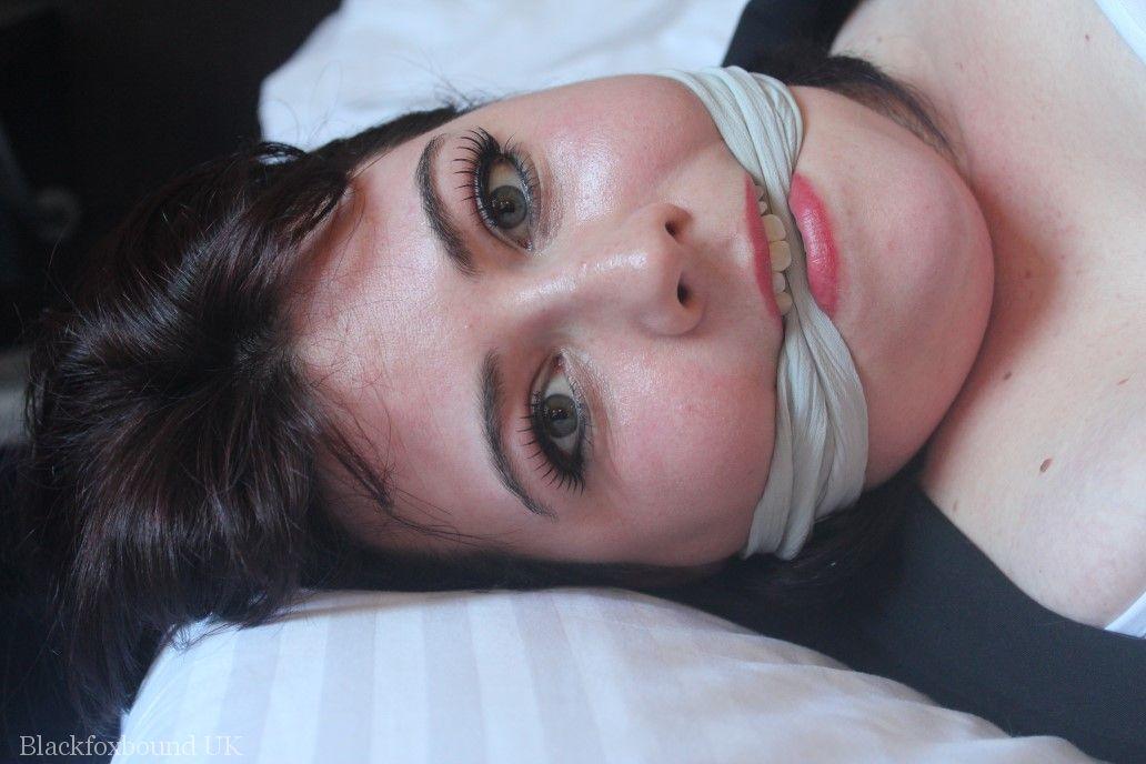 The dark-haired lady exhibits her breasts on a bed, bound and gagged.