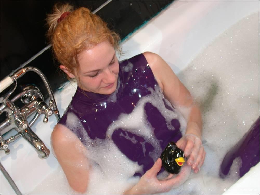 While in the bath, a white girl wears purple latex clothing and displays her bare feet.