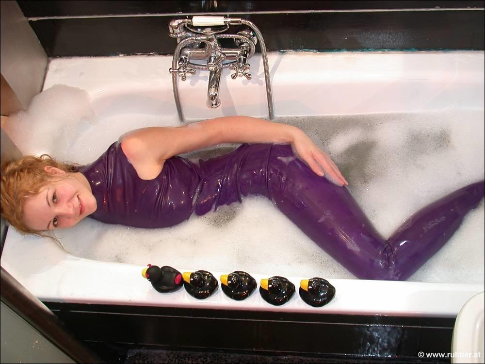 The naked feet of a white girl are observed while she takes a bath in purple latex clothing.