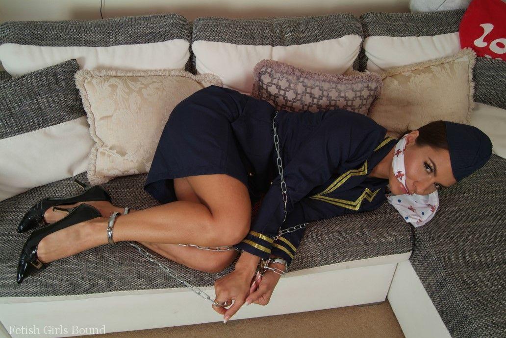 Restricted and gagged: A hot stewardess sits on a sofa in her uniform while being restrained and gagged.