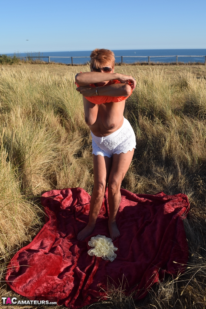 Dimonty, an aged and healthy woman, exposes large natural wonders on a blanket that overlooks the ocean.