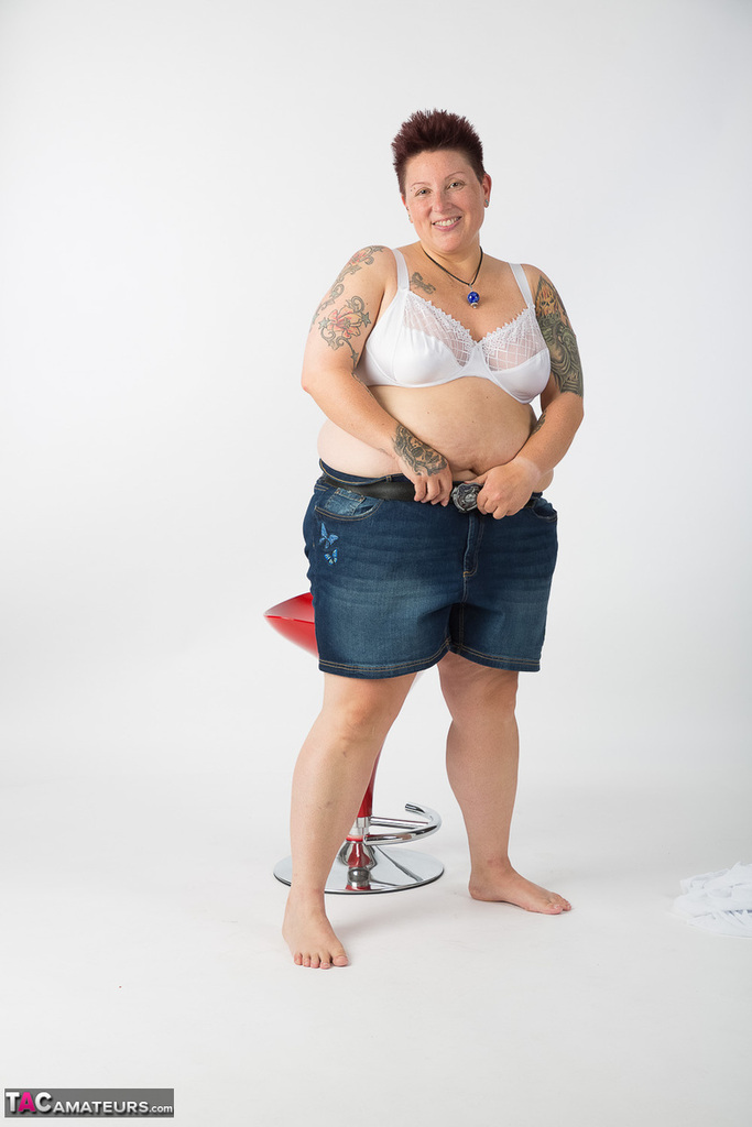 Completely unclothed, the elderly Tattoo Girl takes a seat on a stool after getting naked.