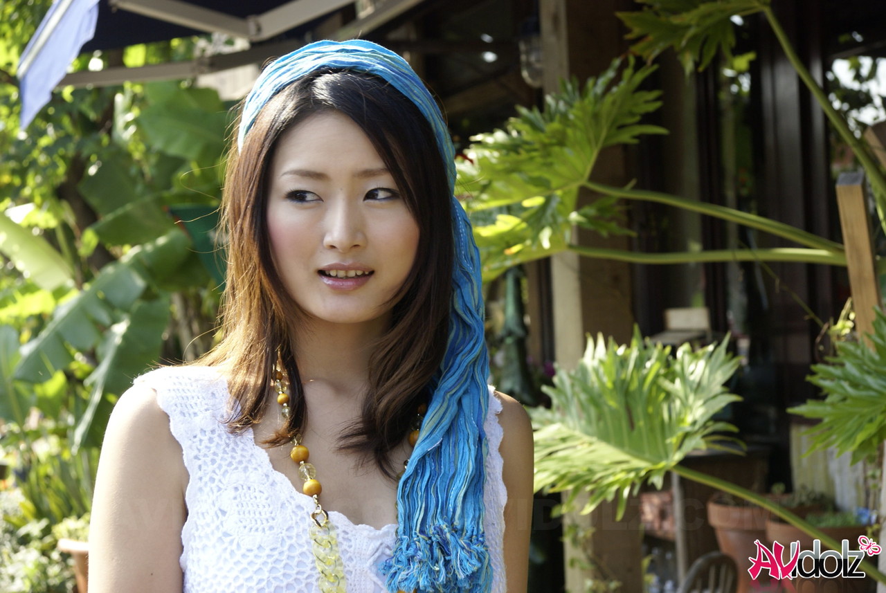 A white dress-clad Asian girl walks into the ocean to her knees.