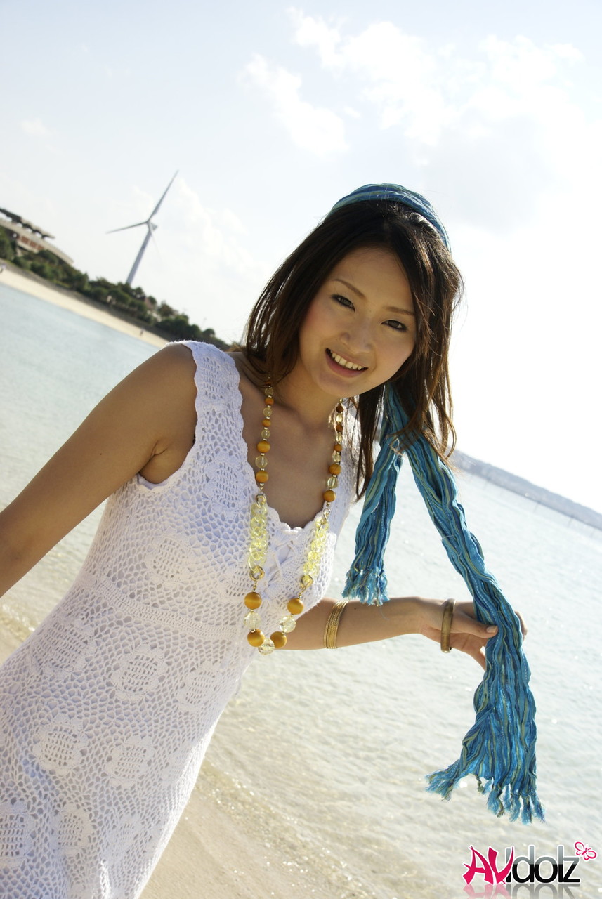 Wearing a white dress and dancing in the water, an Asian girl ventures into the ocean to her knees.