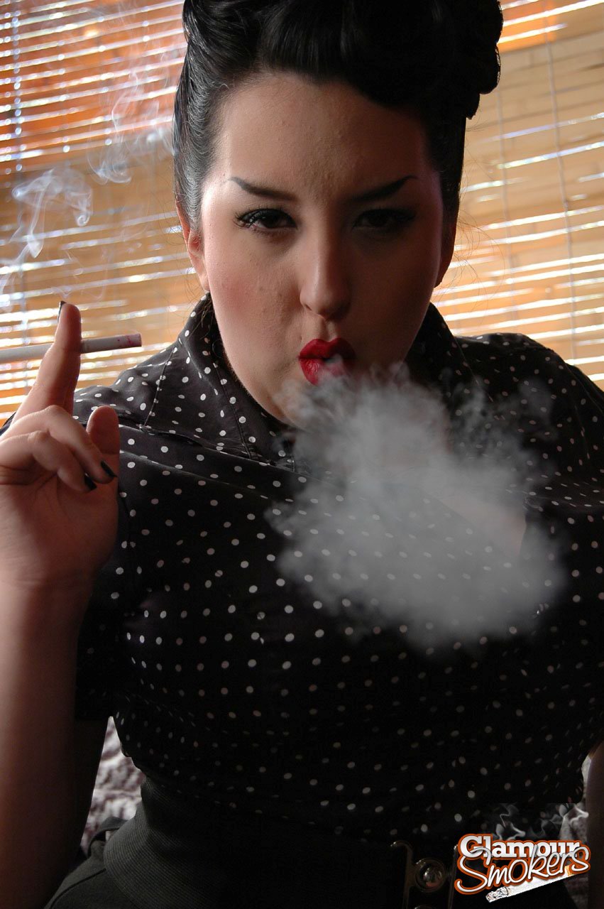 With her face fully clothed and bare, an obese woman consumes Kerosene while holding up a cigarette in her red lips.