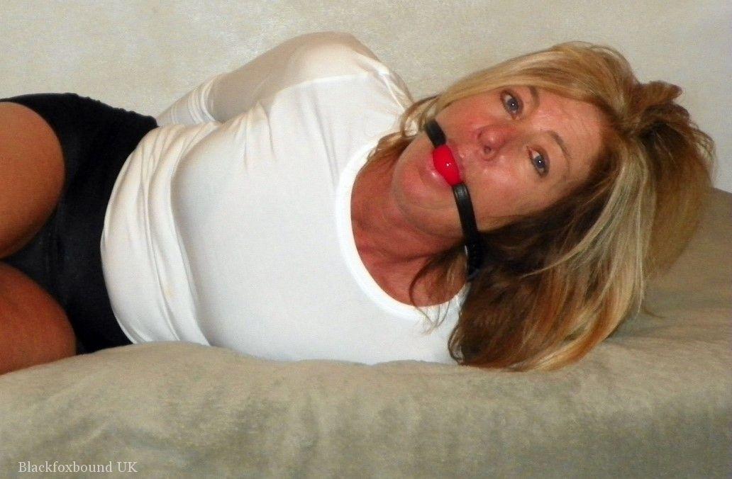 In a bed in black miniskirts, a little-known blonde MILF is held tightly and ball gagged.