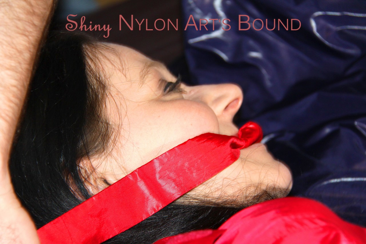 Wearing sexy red shiny nylon shorts and a bright orange shirt, Lucy tied and gagged on the bed with her hands tied.