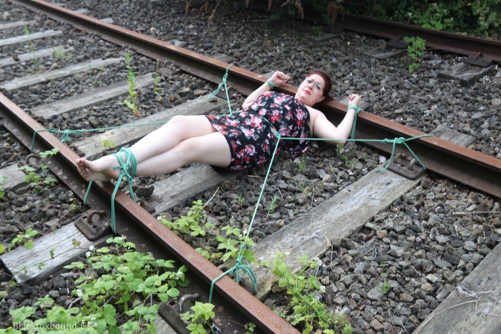 The train tracks are anchored to the head of a natural redhead while wearing a dress and glasses.