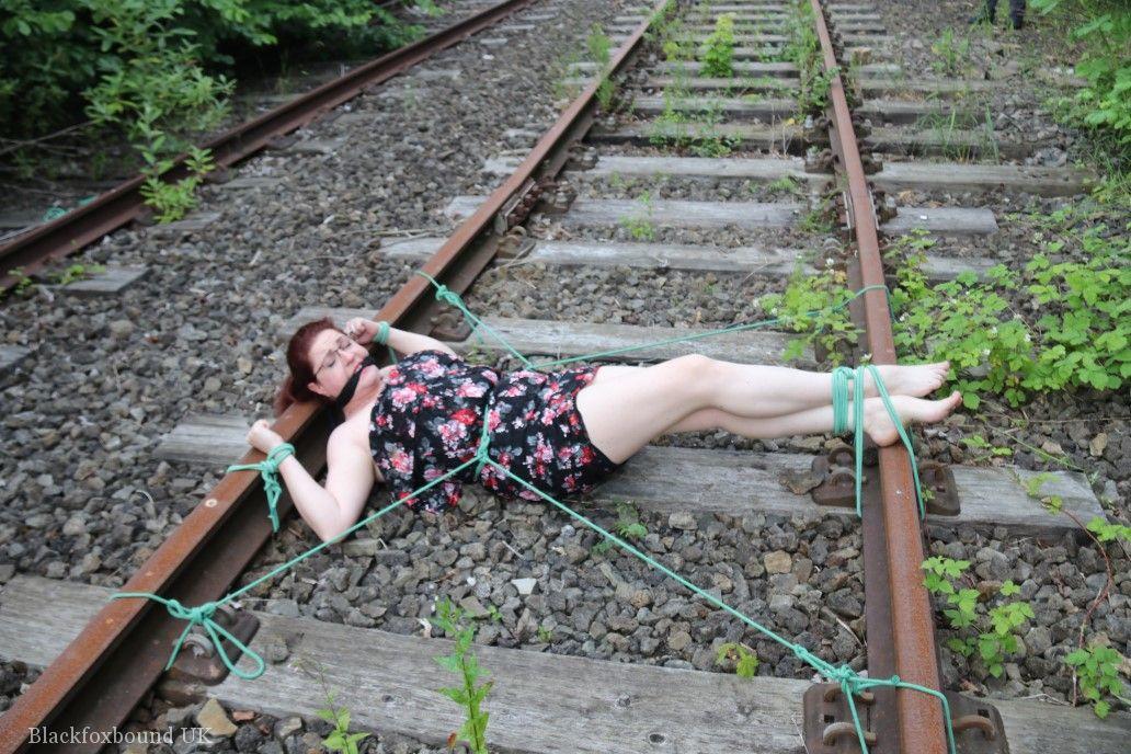 The train tracks are anchored to the head of a natural redhead while wearing a dress and glasses.