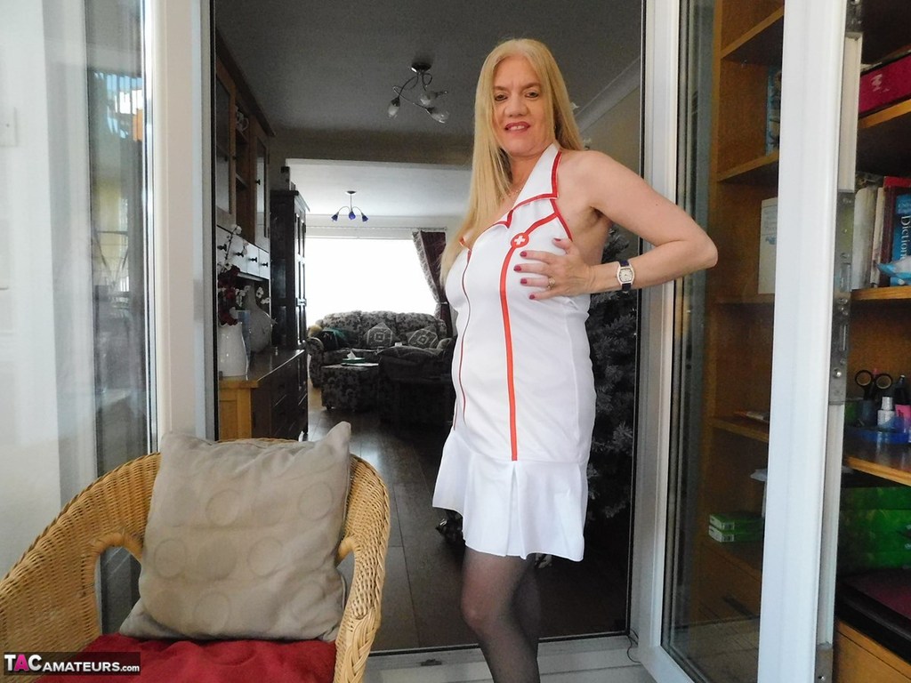 Older British nurse Lily May unzips her uniform on a wicker chair porn photo #422890175