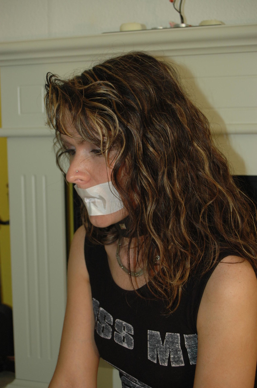 The revealing girl removes the tape from her mouth while being restrained with handcuffs.