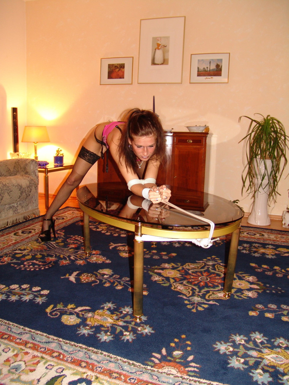 A white girl exhibits a cleave gag while being restrained with rope over a coffee table.