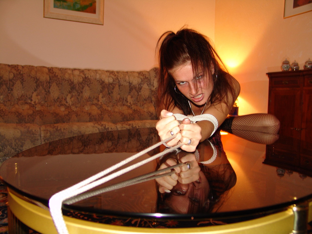 A coffee table is adorned with an exposed rope and a white girl sporting a cleave gag.