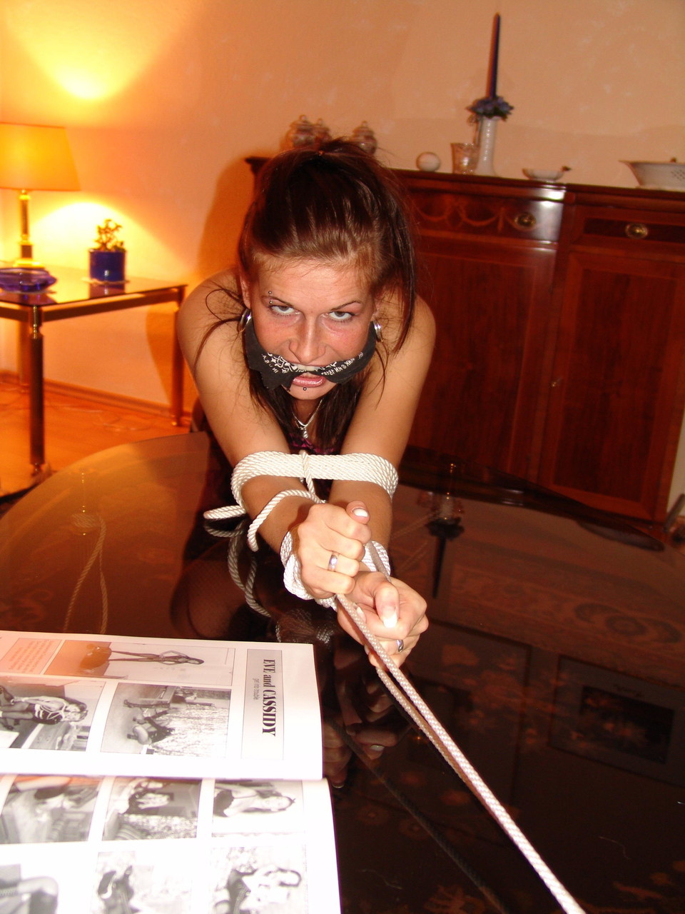 Rope tied over a coffee table: A white girl wears the ‘cleave gag’.