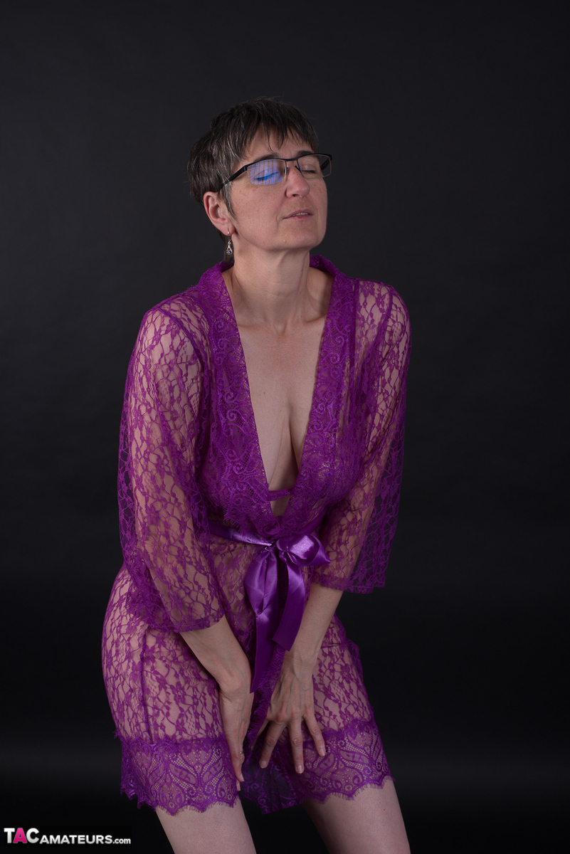 Modeling in purple lingerie, the elderly individual sports short hair and does not wear makeup.