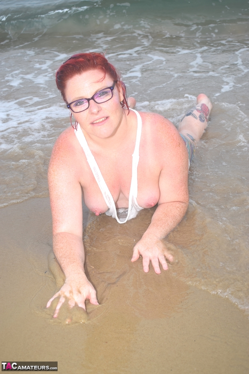 Exposed woman with tattooed red hair wades into the sea before exposing herself.