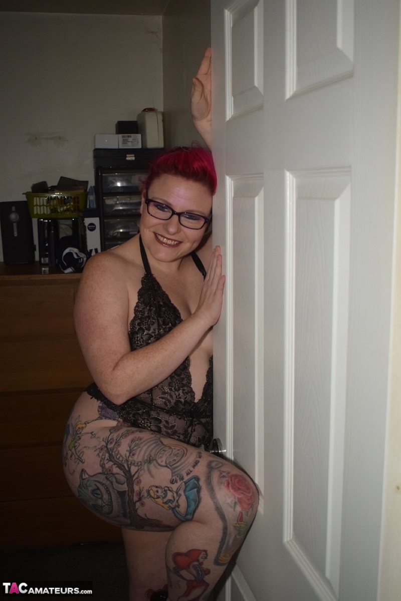 Mollie Foxxx, an amateur with tattoos, models herself in black lingerie while wearing glasses.