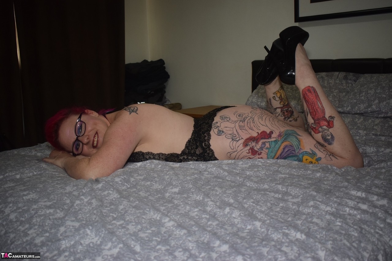 Tattooed amateur Mollie Foxxx poses in black lingerie while wearing glasses.