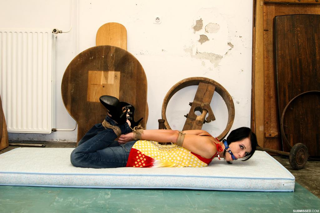 Dressed-up woman with dark hair struggles against her rope restraints.