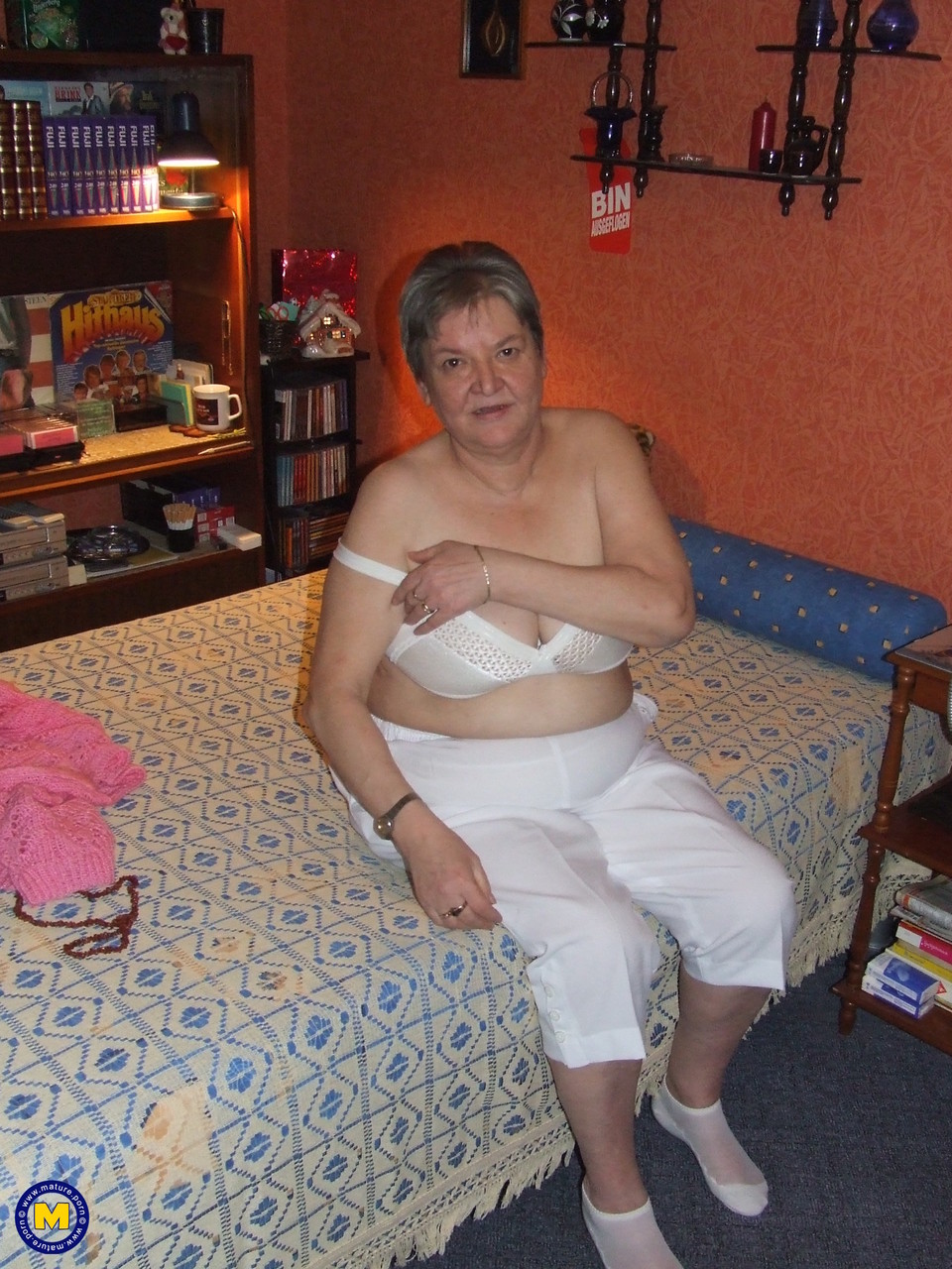 Uschi, a fat grandma, puts on her clothes, poses in the nude, and pleases on a bed.