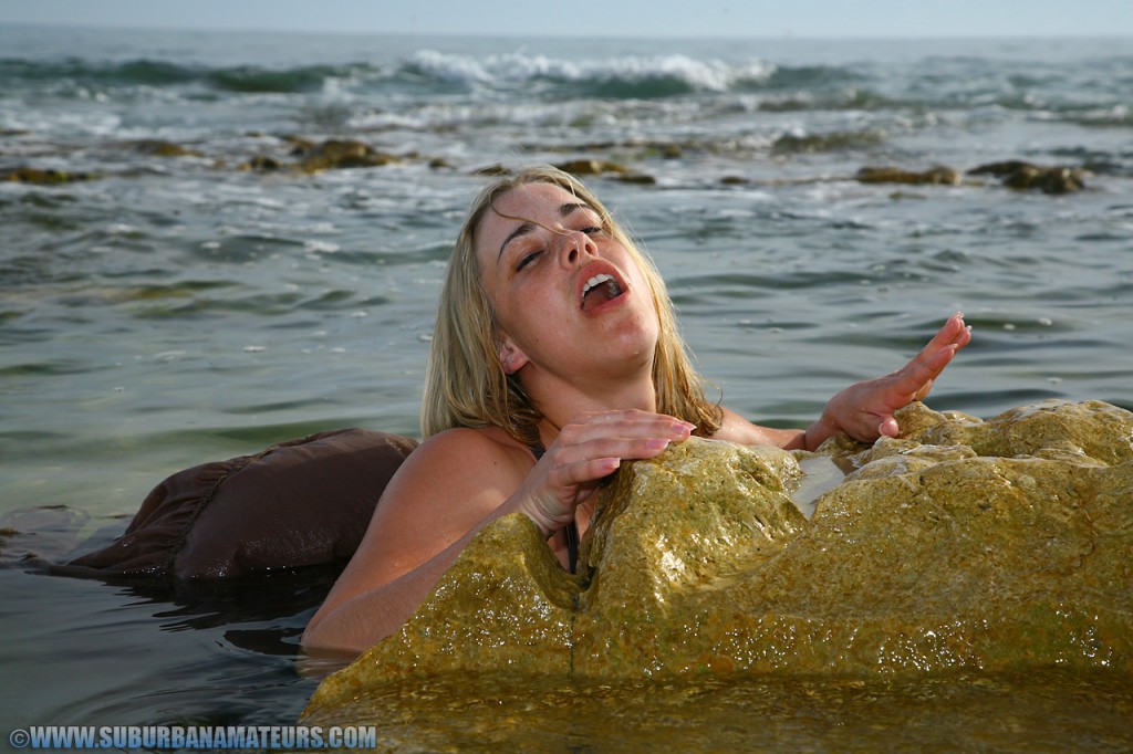 The British model Tammy Oldham engages in provocative self-pleasure while posing on a sandy beach.