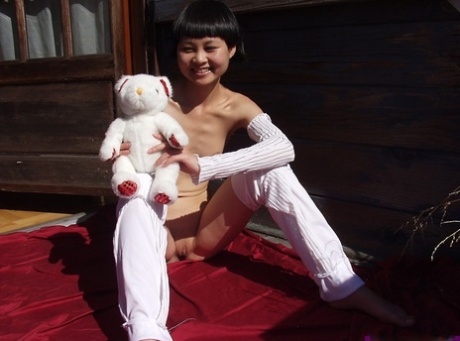 Cute Asian teen holds a plush toy after getting naked during solo action