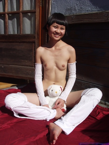 Cute Asian teen holds a plush toy after getting naked during solo action