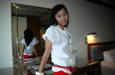 In a hotel room, an Asian girl who appears young strips for a sexual tourist.