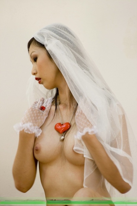 The beautiful and elegant Asian bride is seen wearing a veil while sipping on bubbles from a bottle inside her veil.