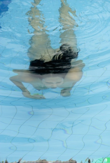 At the bottom of a pool, an Asian girl with firm hands and breasts swims naked.