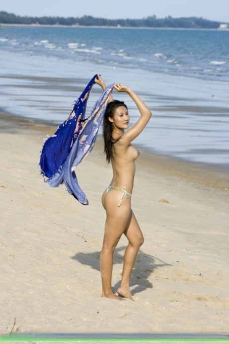 In her bikini bottoms, an Asian girl explores a beach while walking along the shore.