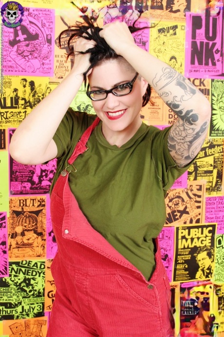 A trimmed pussy is held by Michelle Aston, who has tattoos on her body, during solo action.