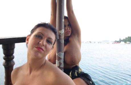 Lesbian women Kora Kryk and Anete Bueno display their sizable breasts to a passing vessel.