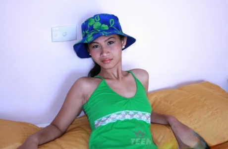 Skinny Filipina teen gets naked on a bed while wearing a bucket hat