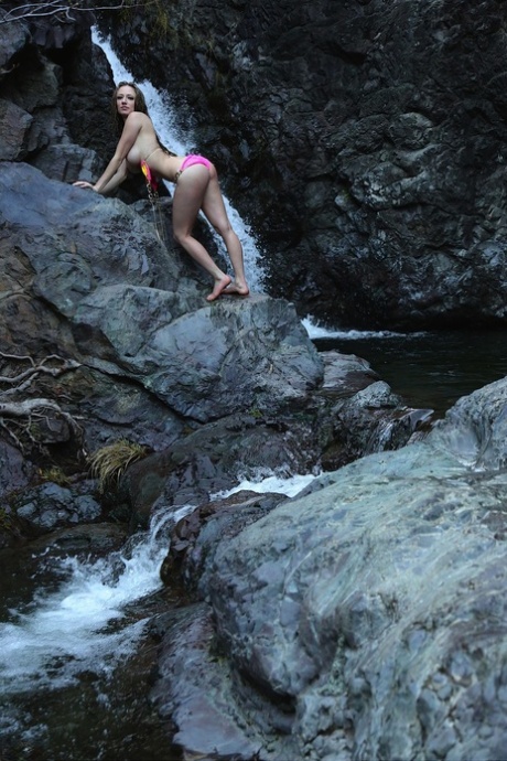 Caucasian girl: Lily Xo removes her bikini top as she stands in front of a waterfall.