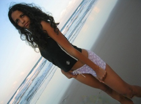 Polliana, a small Brazilian girl, is seen wearing a tank top and lifting it up while lounging on the beach.