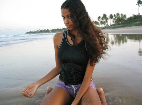 On the beach, Polliana stands tall with her barefooted body while wearing a tank top.