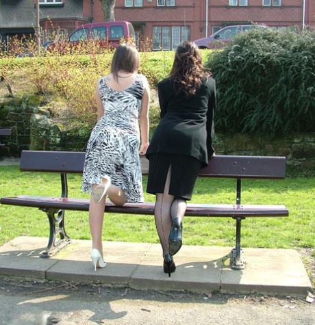 Clothed Females Admire Each Other High Heeled Shoes On A Park Bench