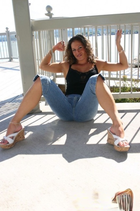 A female amateur posing nude on a balcony in denim capris is observed.